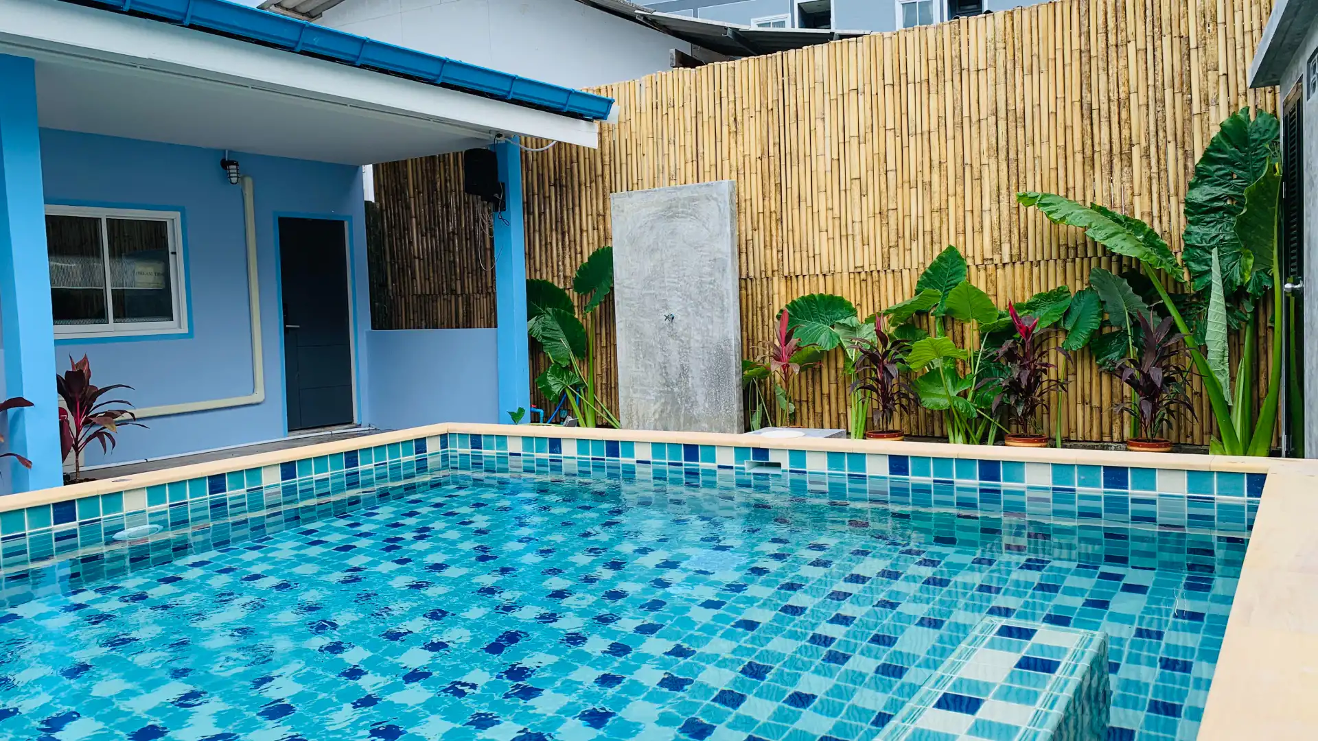 dark and light blue house with a pool some plants and a fence outside